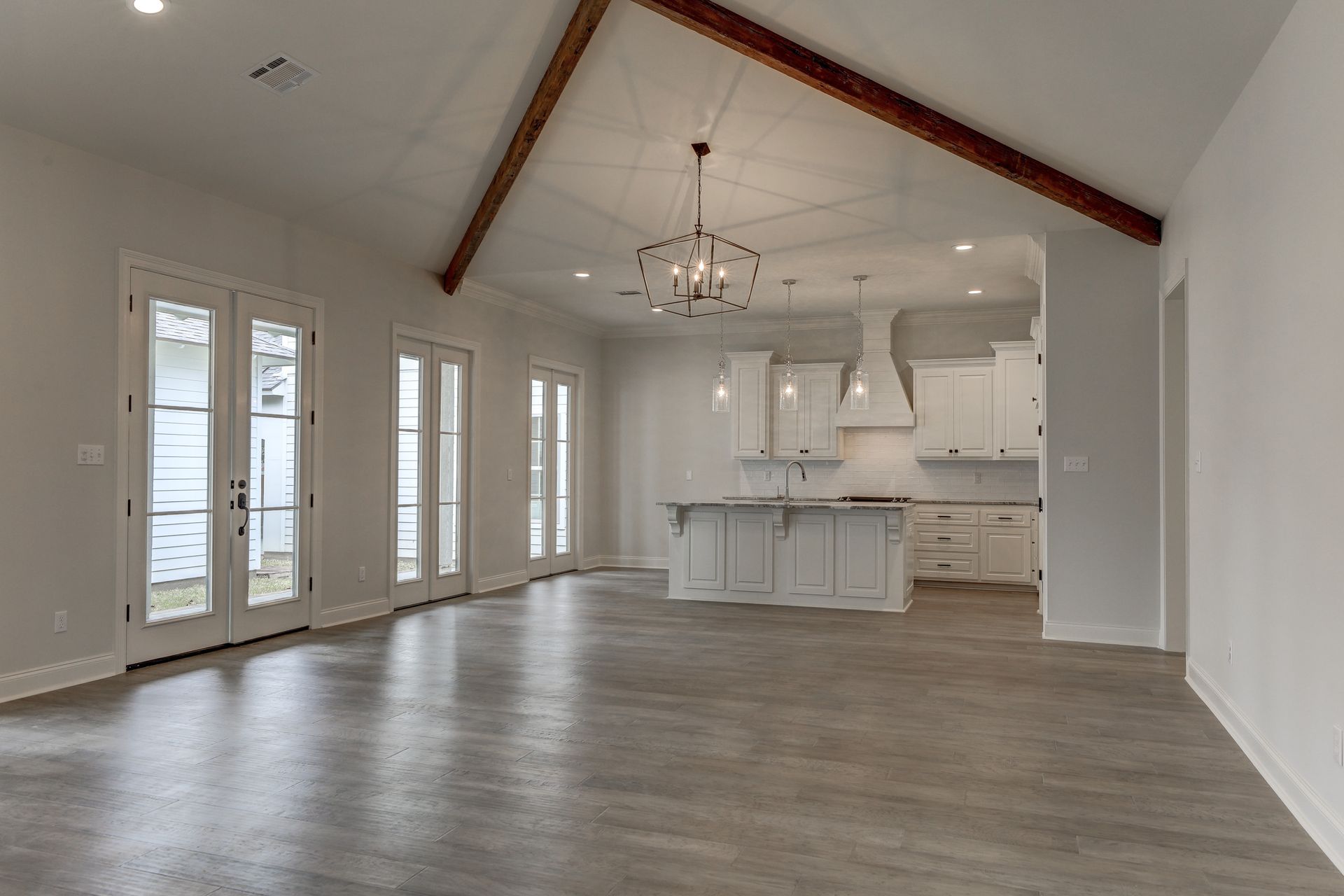 A large empty room with hardwood floors and a kitchen in the background.