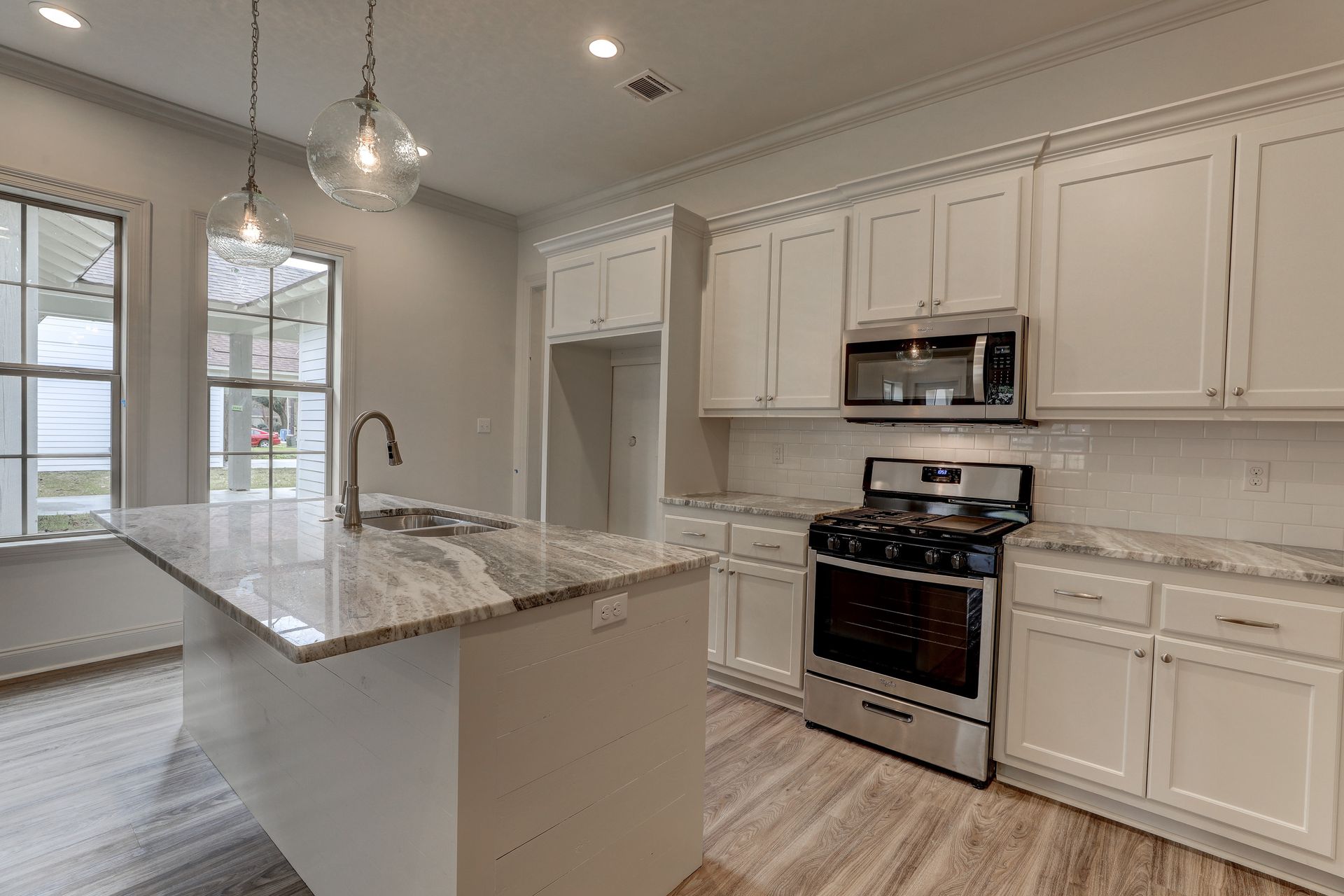 A kitchen with white cabinets , stainless steel appliances , granite counter tops and a large island.