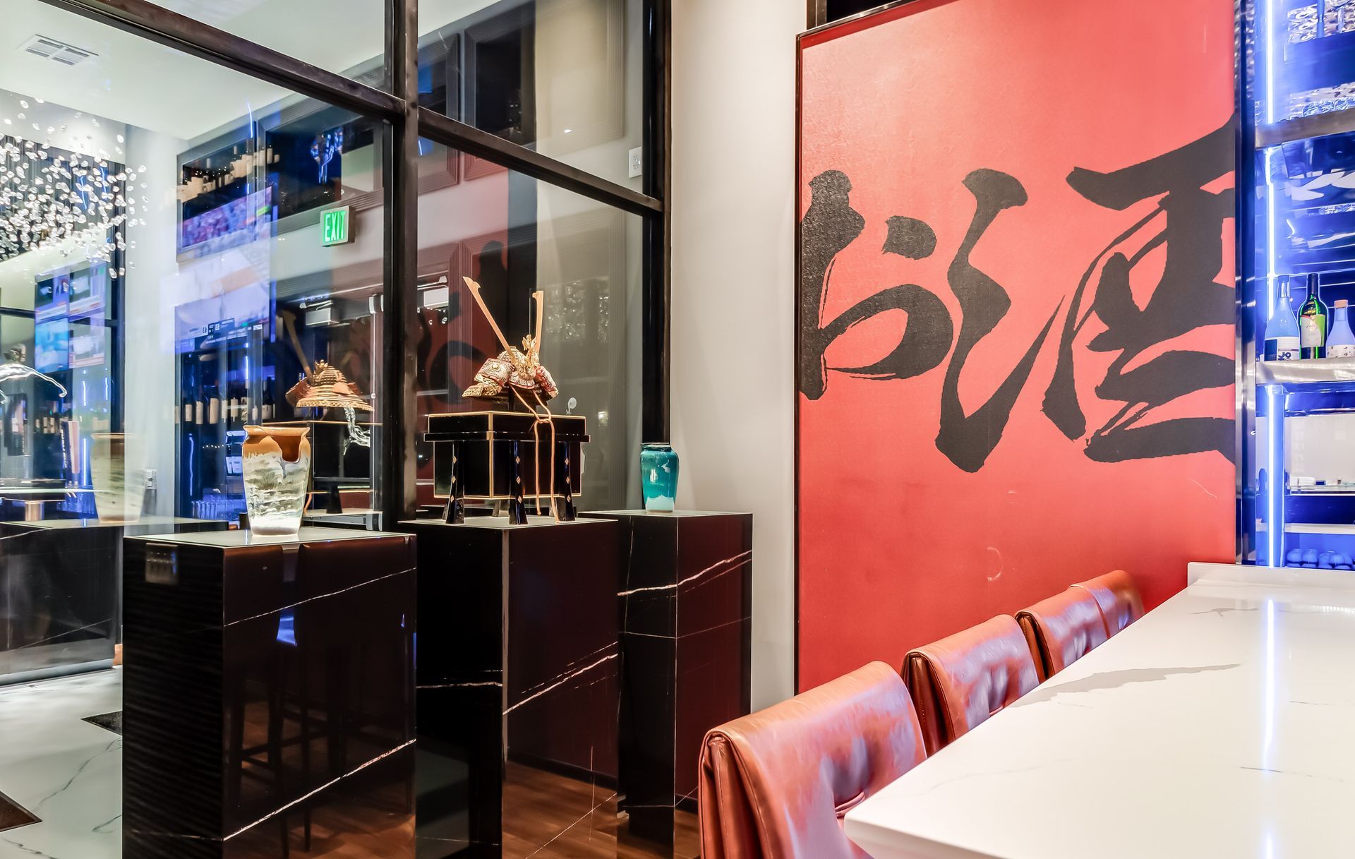 A restaurant with a long table and chairs and a red wall with chinese writing on it.
