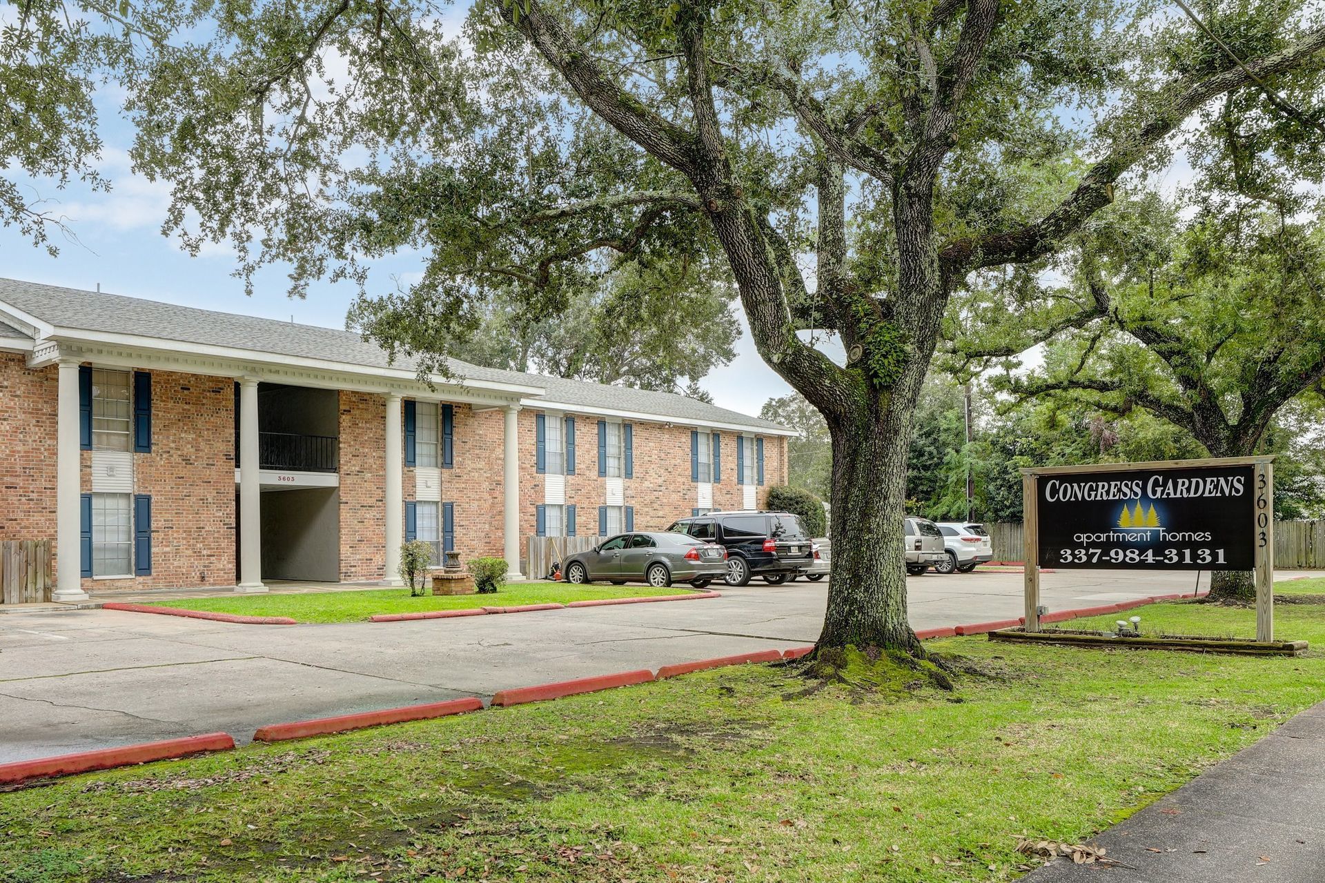 A brick apartment building with cars parked in front of it and a sign in front of it.