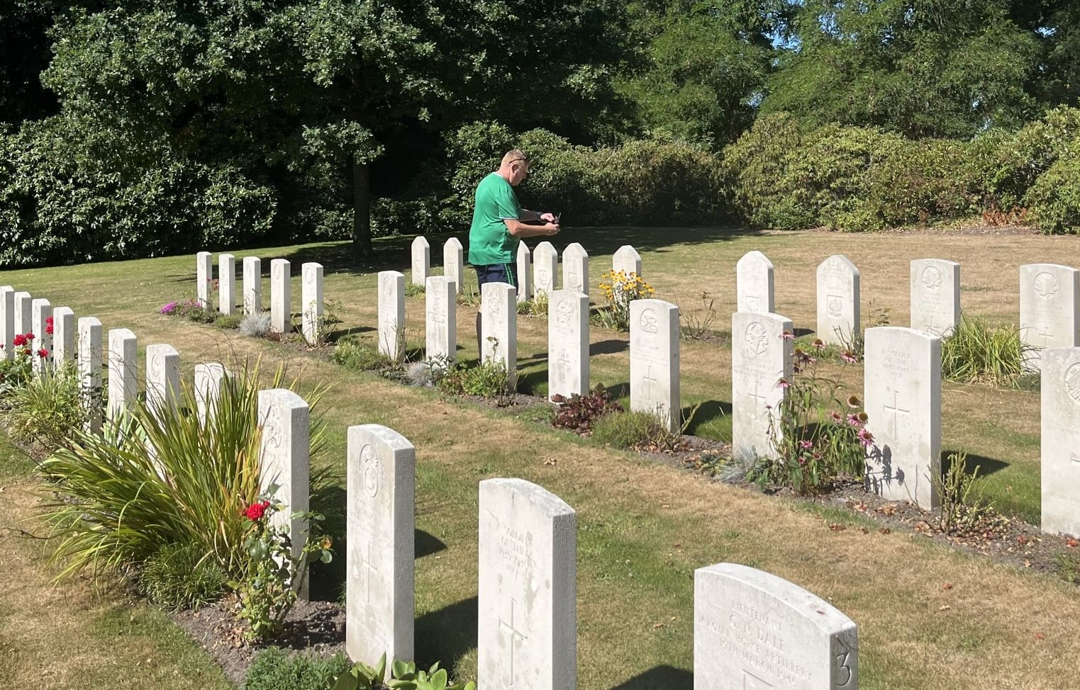 Een man in een groen shirt staat op een begraafplaats.