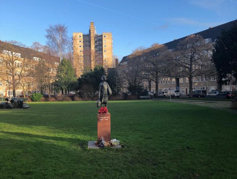 A statue of Anne Frank in a park with a building in the background