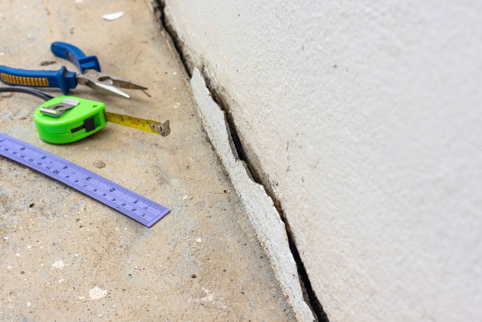 A measuring tape , pliers , and a ruler are on a concrete surface.