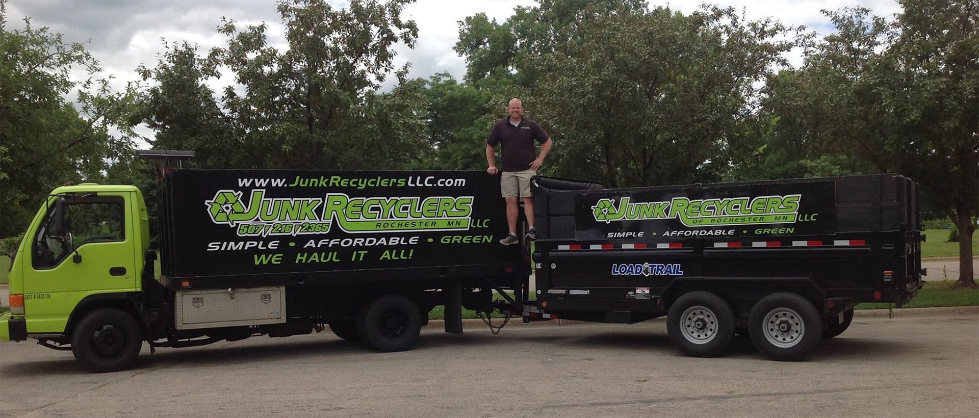 A lime-green dump truck and trailer with a man standing on it; trees are in the background.