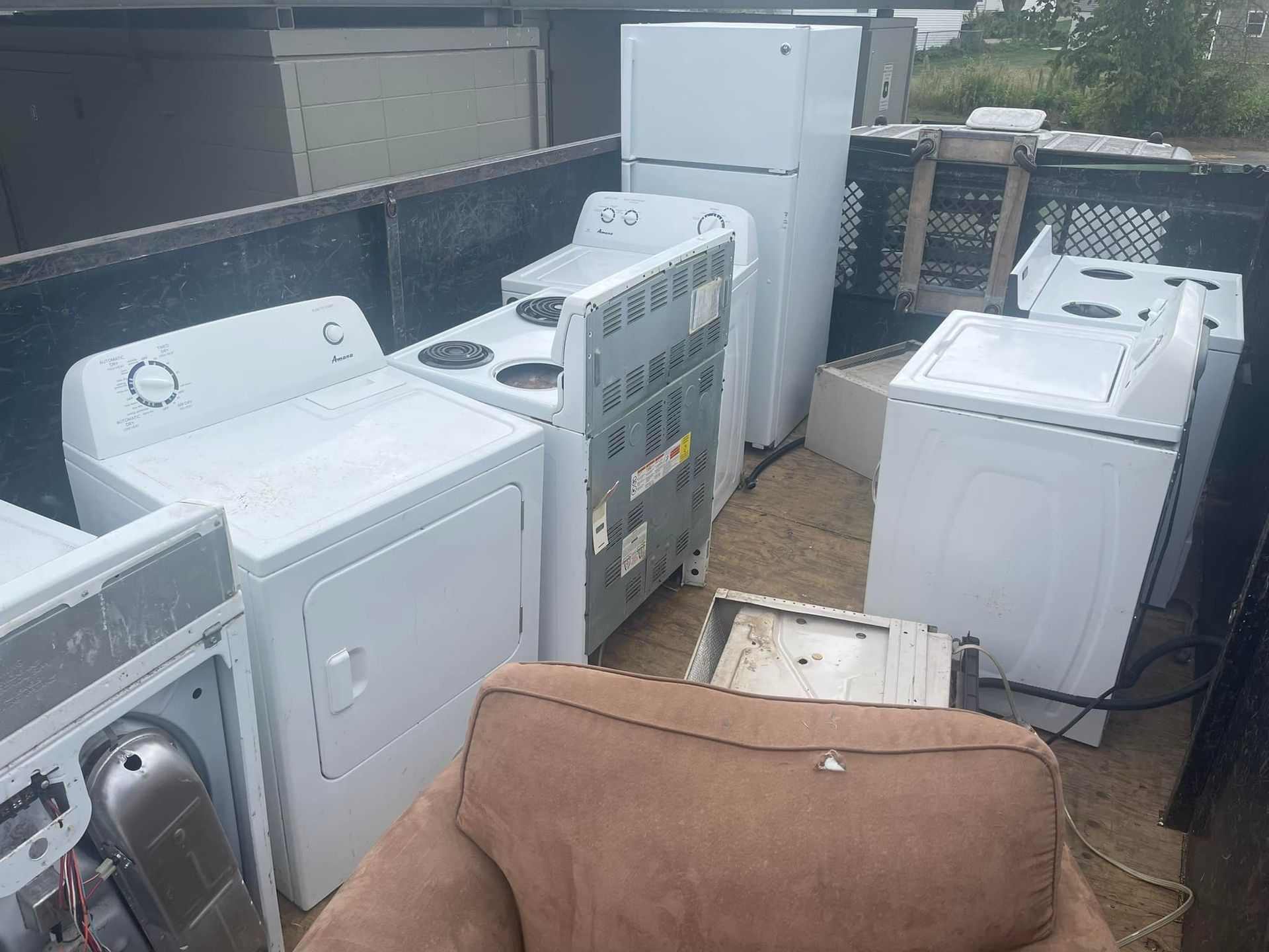 A truck bed filled with several white appliances, including a refrigerator, washer, dryer, and stove