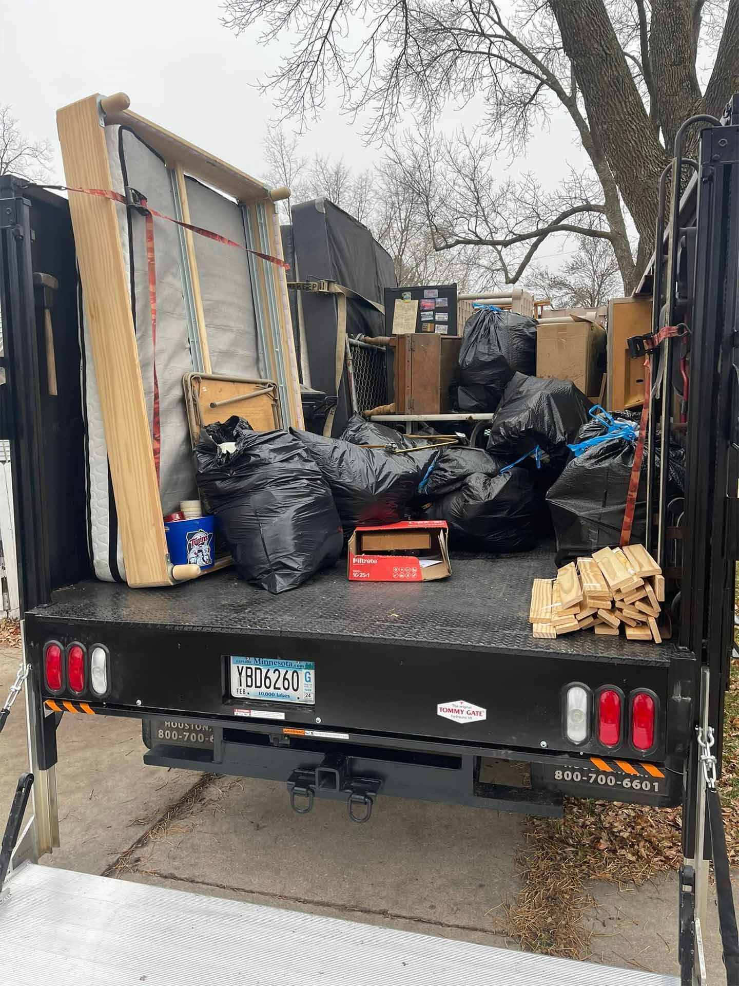 A truck bed filled with trash bags, a mattress, and other discarded items