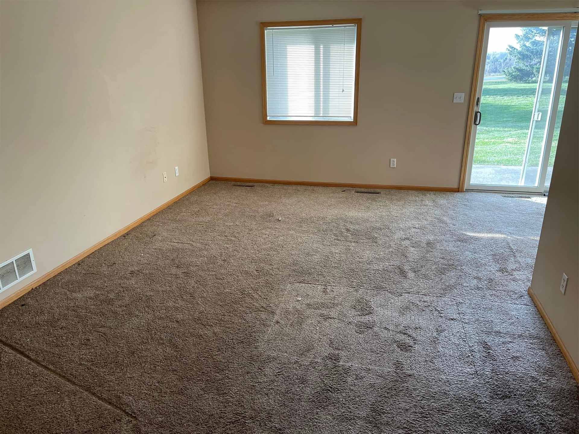 Empty room with brown carpet, beige walls, window with blinds, and sliding glass door to outside.