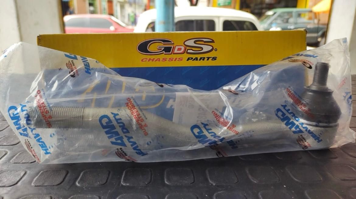 Rótula de dirección en embalaje de plástico, con una caja de marca amarilla y azul en el fondo.