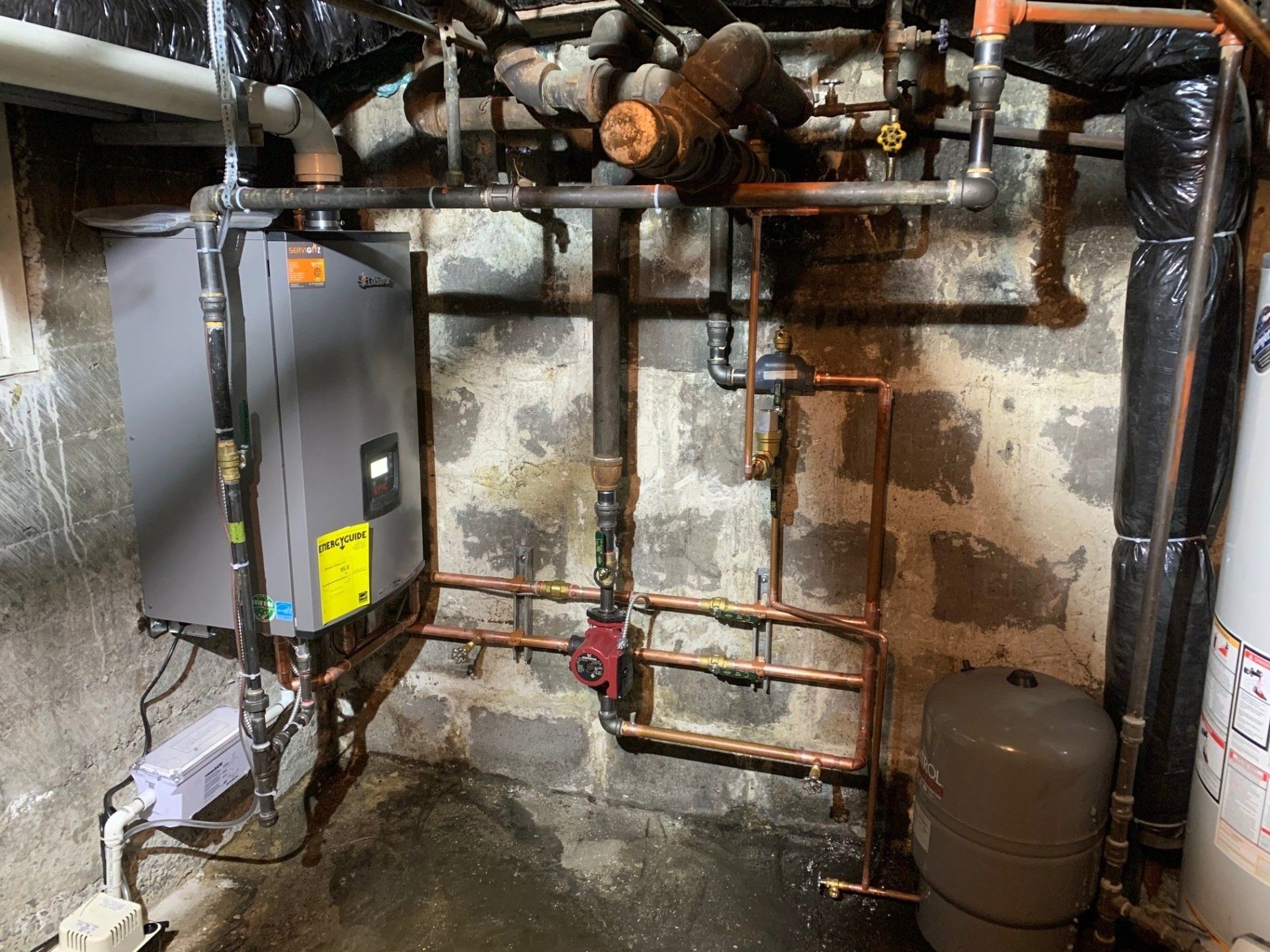 Une chaudière est installée dans un sous-sol à côté d'un chauffe-eau.