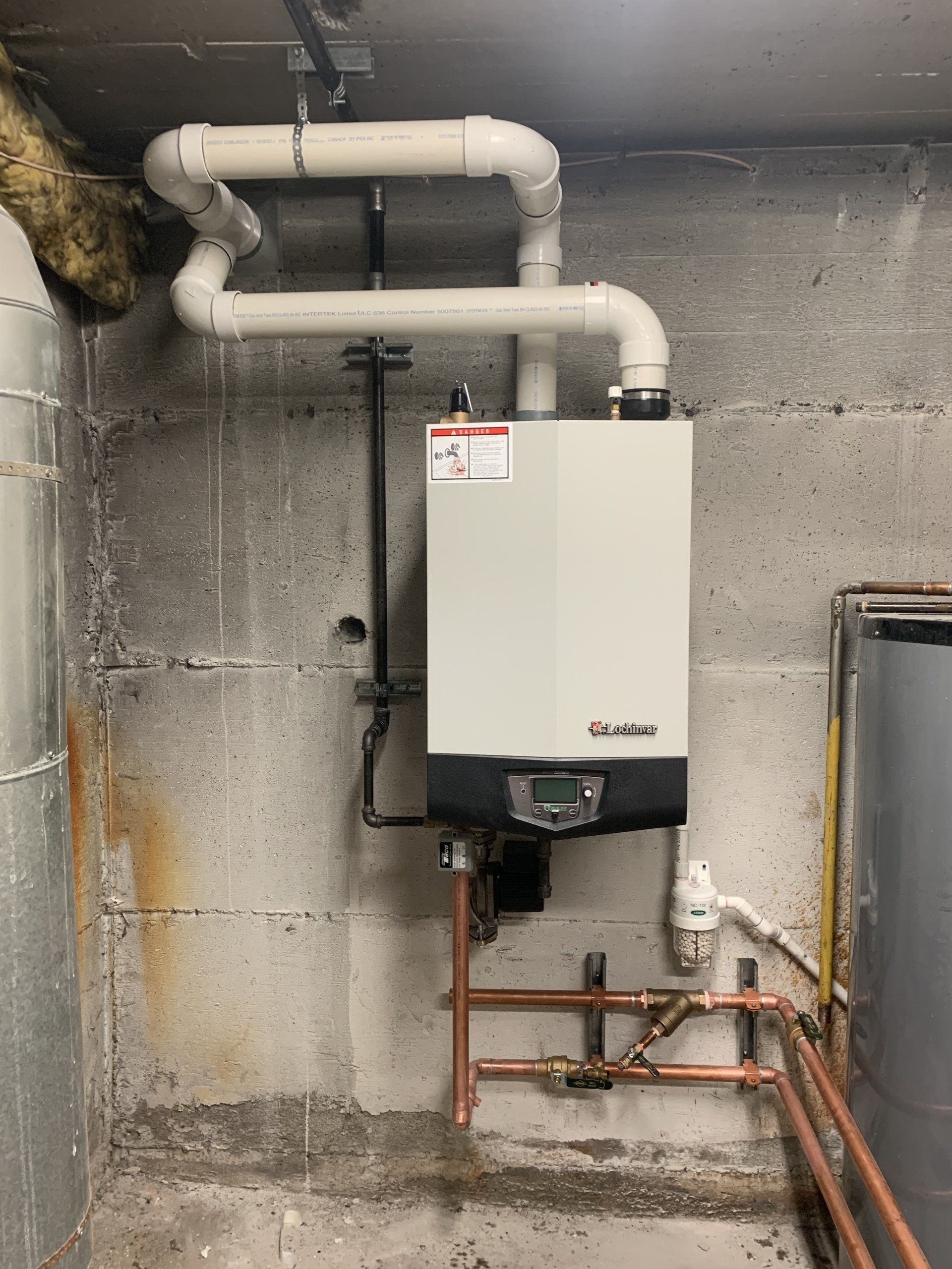 Une chaudière est accrochée à un mur en béton dans un sous-sol.