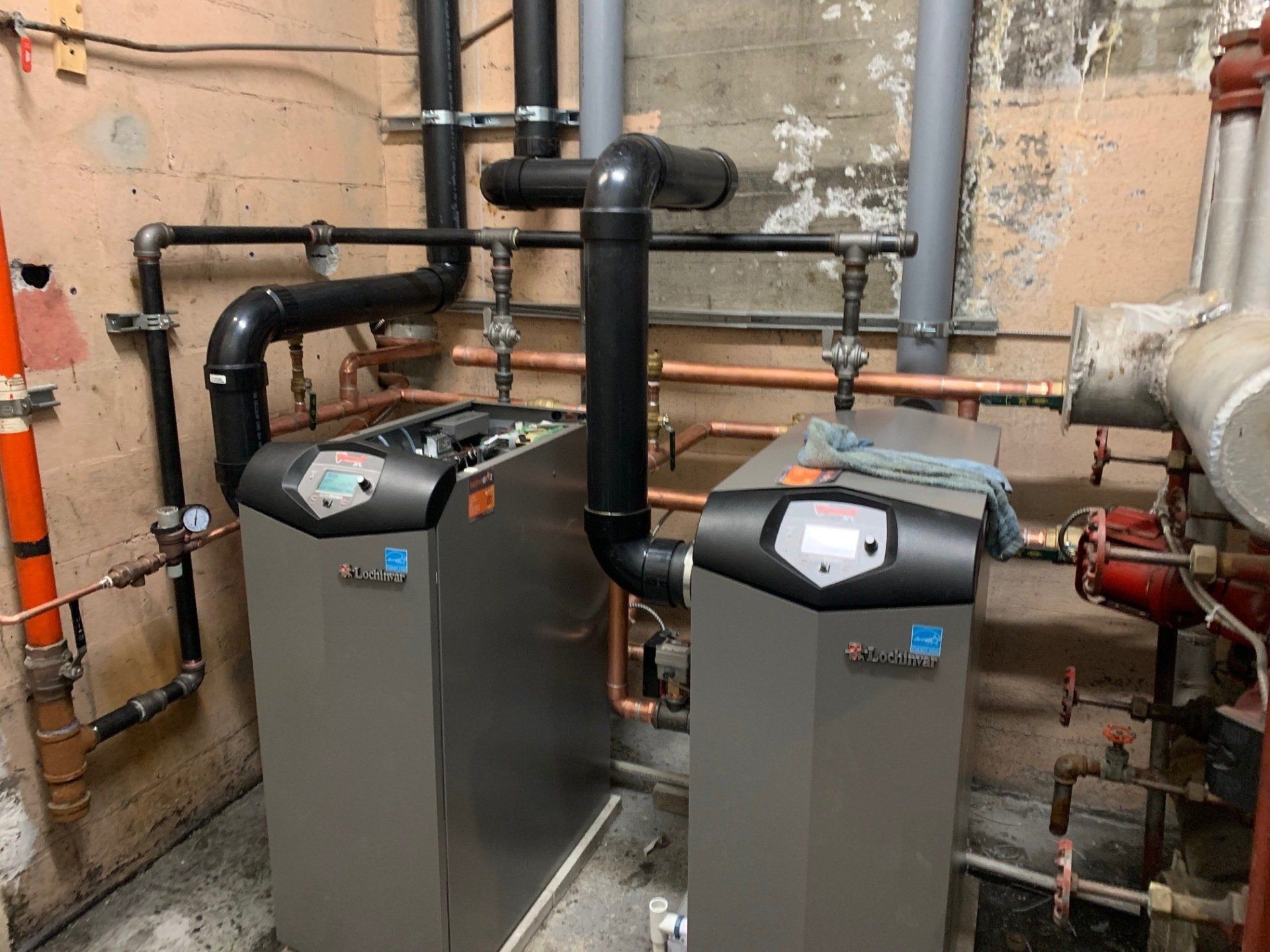 Deux chaudières sont placées l'une à côté de l'autre dans une pièce avec des tuyaux.