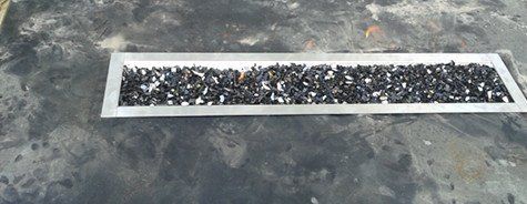 Un plateau en métal rempli de gravier noir est posé sur une surface en béton.