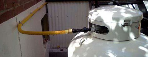 Un réservoir de propane est fixé à un tuyau jaune sur le côté d'un bâtiment.