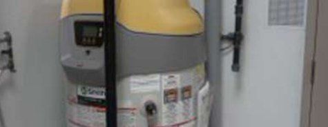 Un chauffe-eau jaune et gris est posé à côté d'un mur blanc.