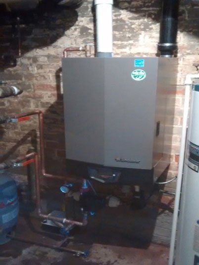 Une chaudière est installée dans un sous-sol à côté d'un mur de briques.