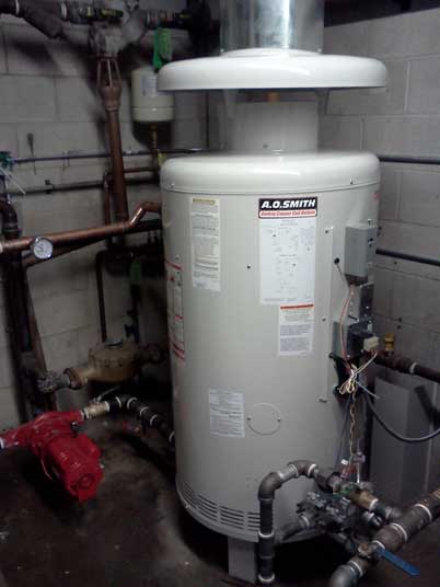 Un grand chauffe-eau blanc se trouve dans une pièce avec des tuyaux.