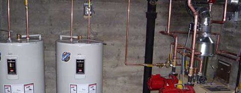 Deux chauffe-eau sont assis l'un à côté de l'autre dans une pièce avec des tuyaux en cuivre.