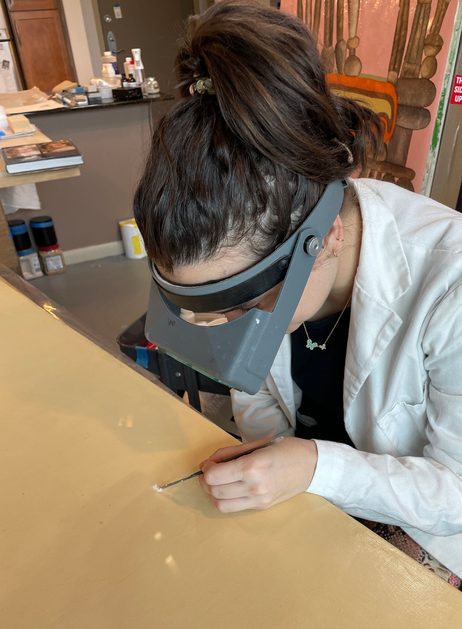 A woman wearing a magnifying glass is working on a piece of wood.
