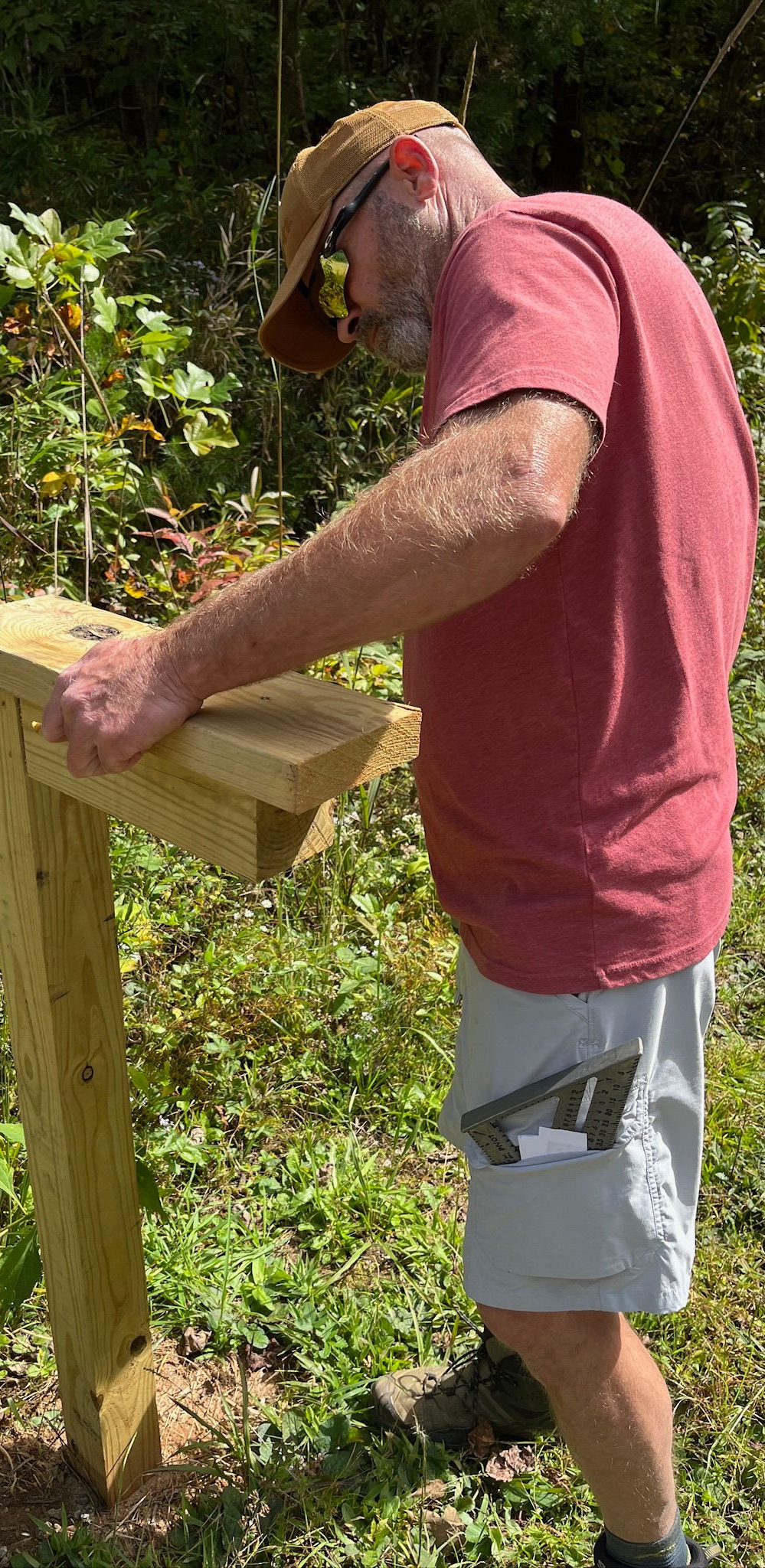 A man wearing a hat and sunglasses is writing on a clipboard.