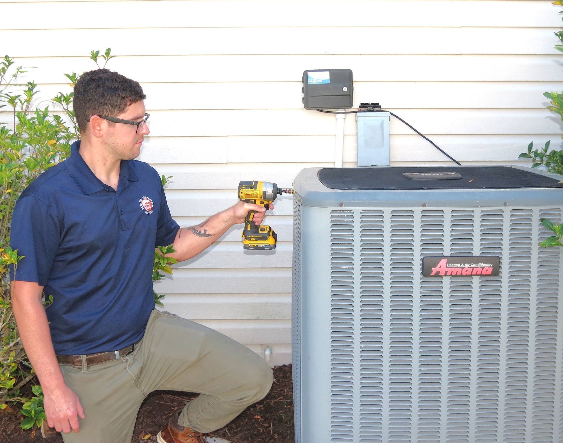 A Carolina Temperature Control HVAC technician using a drill on an air conditioning unit outside a house.