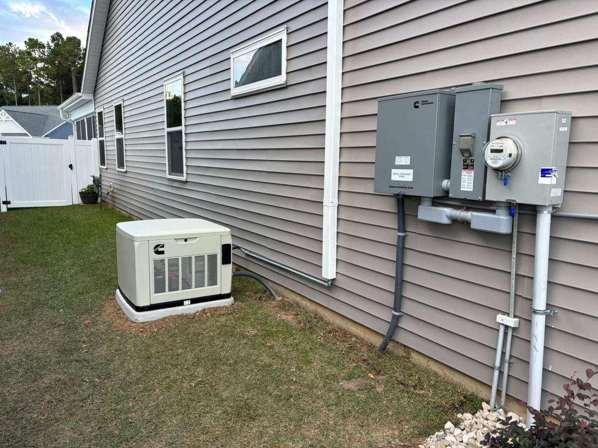 Generator and electrical panel mounted on a house exterior, with a grassy lawn.