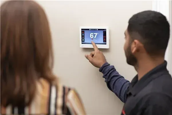 An HVAC technician showing a customer how to work a thermostat