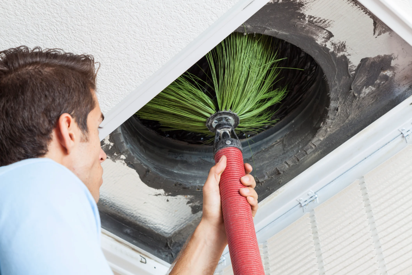 Technician performing a whole-home duct cleaning with a vacuum and brush