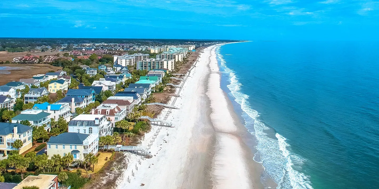 Aerial view of Pawleys Island; a beach with white sand and clear blue water, lined with colorful houses.