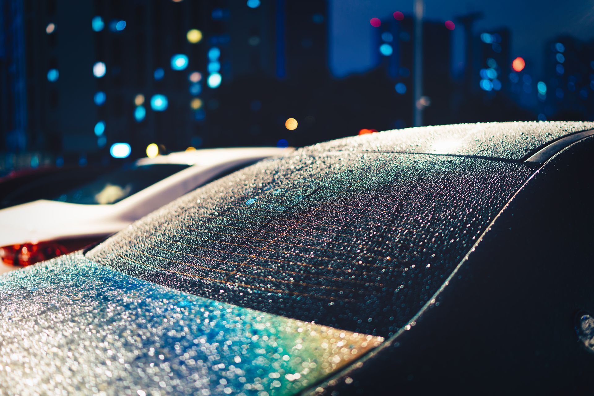A car with rain drops on the windshield is parked in a parking lot at night - Seagrove, NC - Seagrove Glass Shop