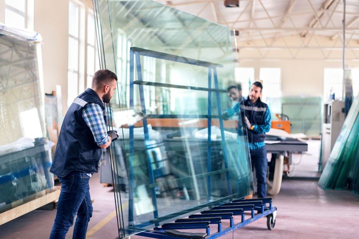 Two men are carrying a large piece of glass on a cart in a factory - Seagrove, NC - Seagrove Glass Shop