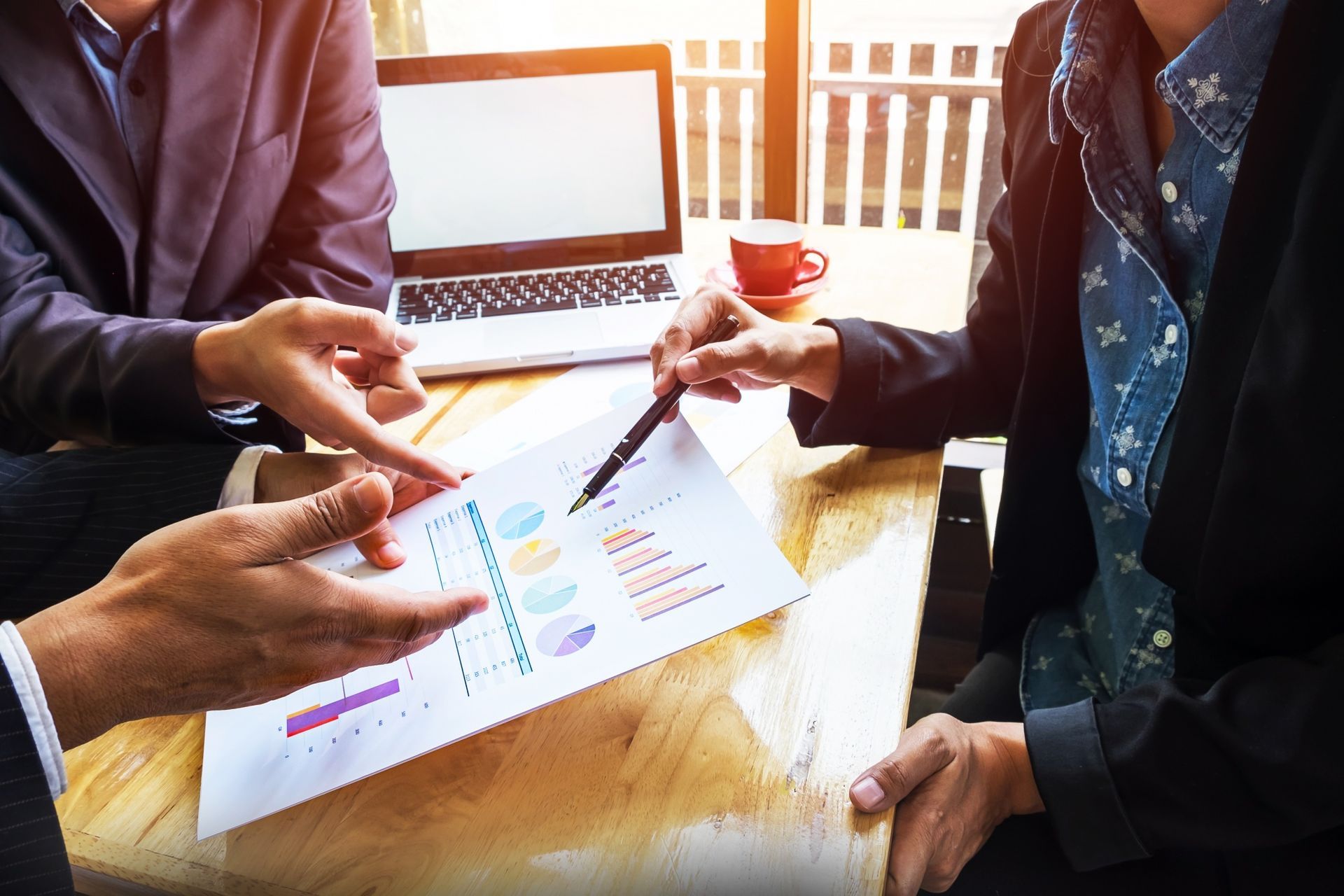 Three people reviewing financial data in a meeting, pointing at charts, and working on a laptop.