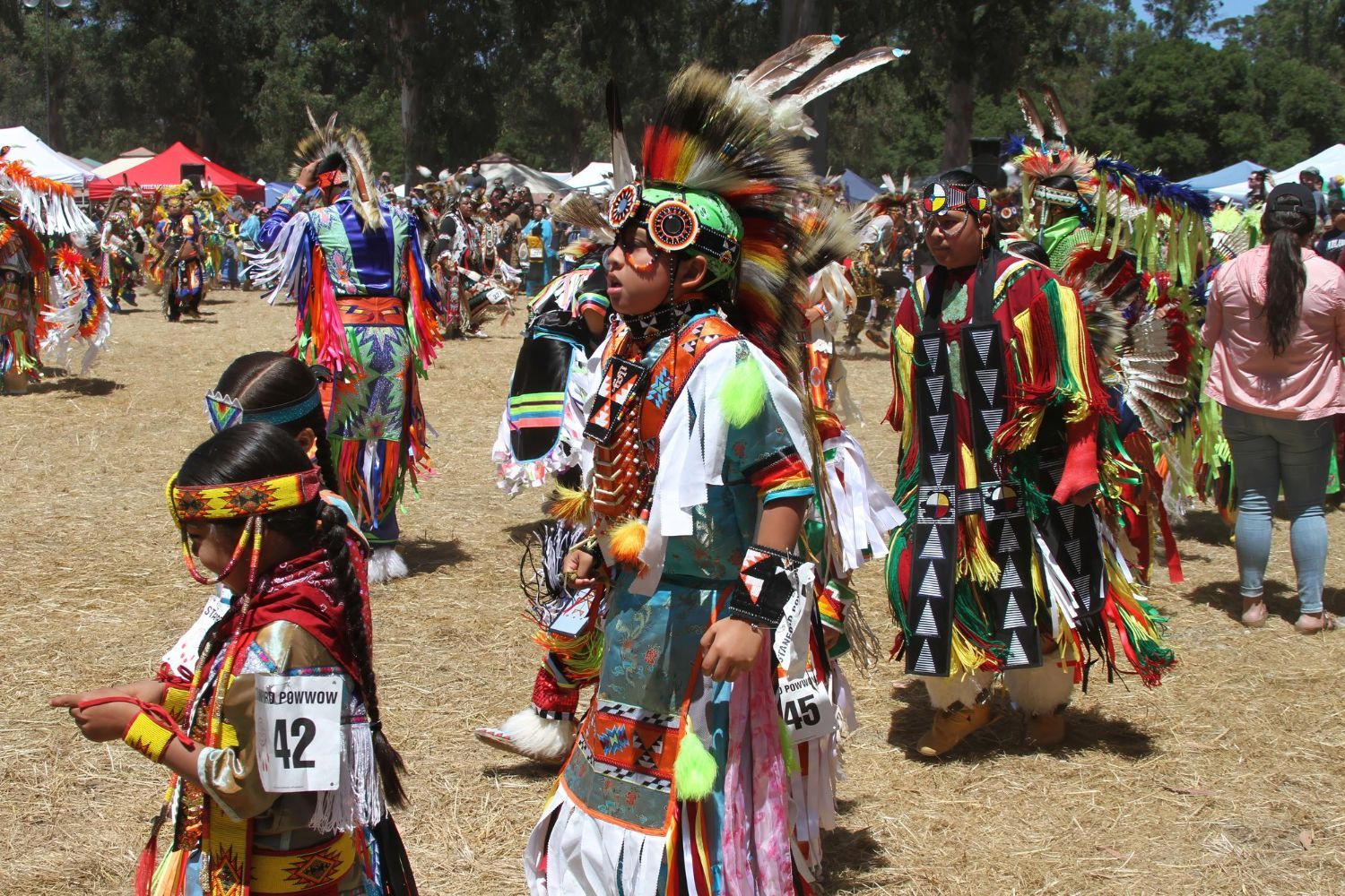 People in vibrant Native American regalia dance outdoors at a Powwow.
