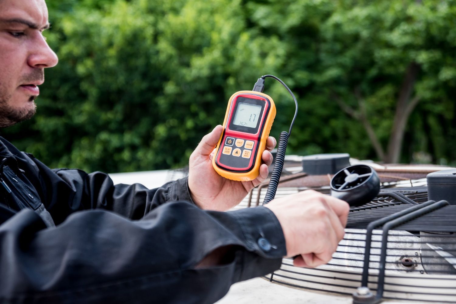 Man using a handheld instrument to measure airflow on an outdoor air conditioning unit.