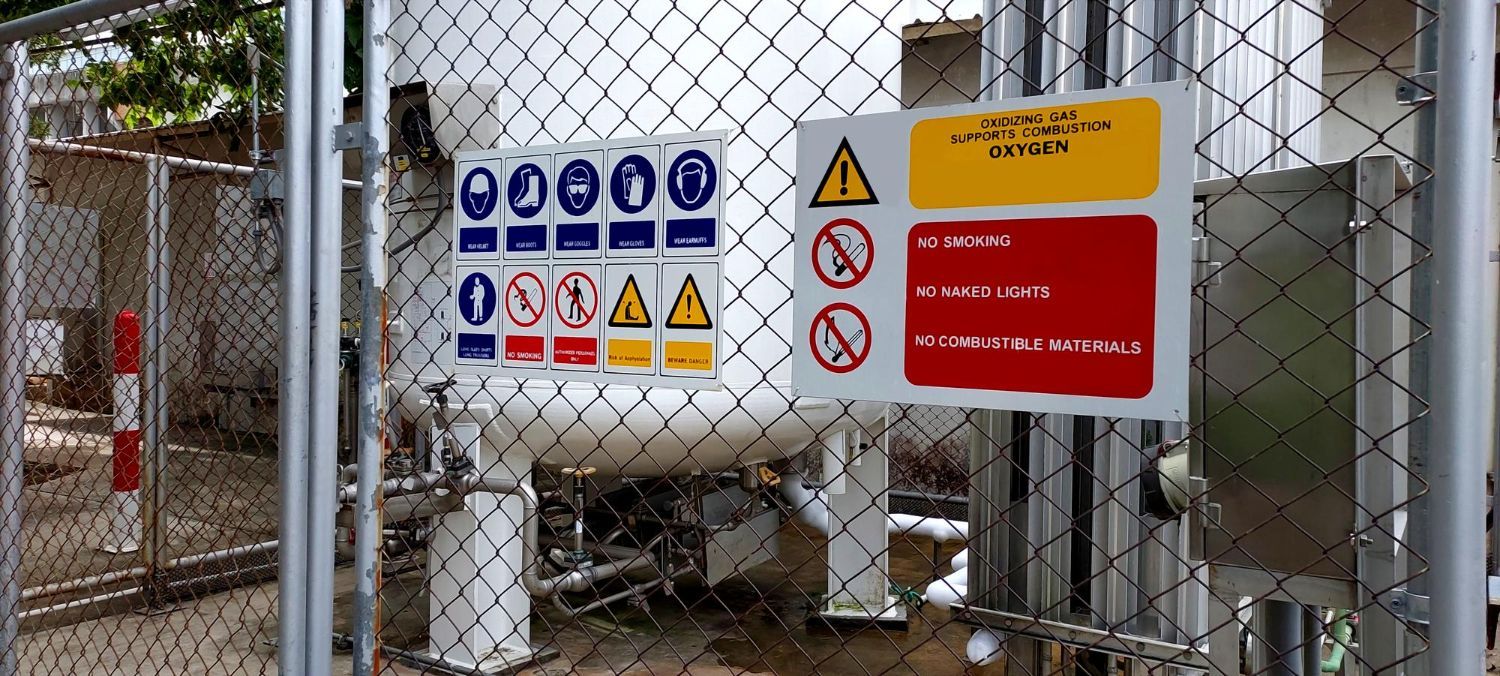 Signs on a fenced industrial area, warning about electrical hazards and restricted access.