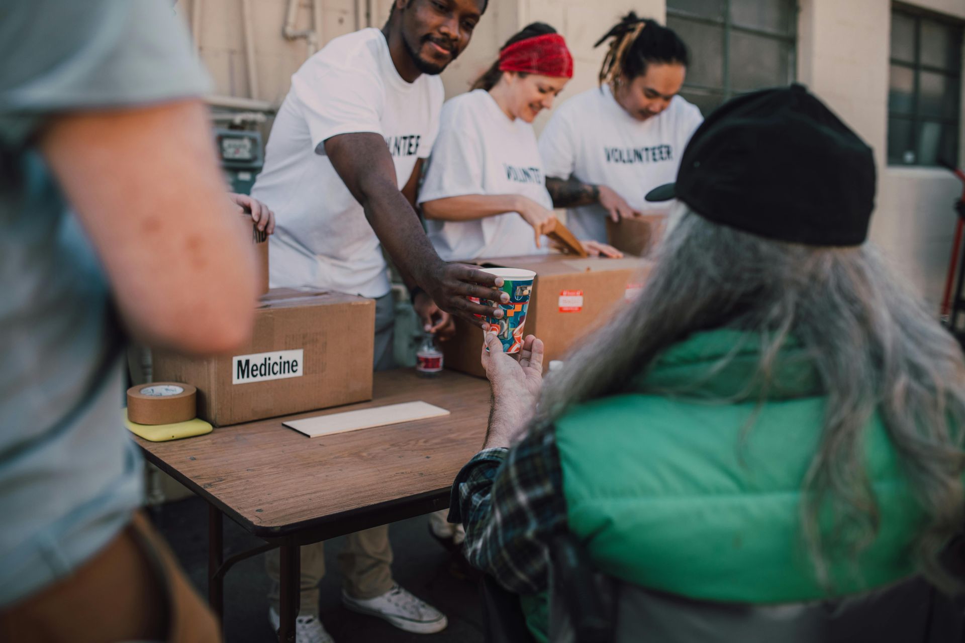 Volunteers distributing boxes to a person seated at a table.  Outdoor setting, all wearing volunteer shirts.