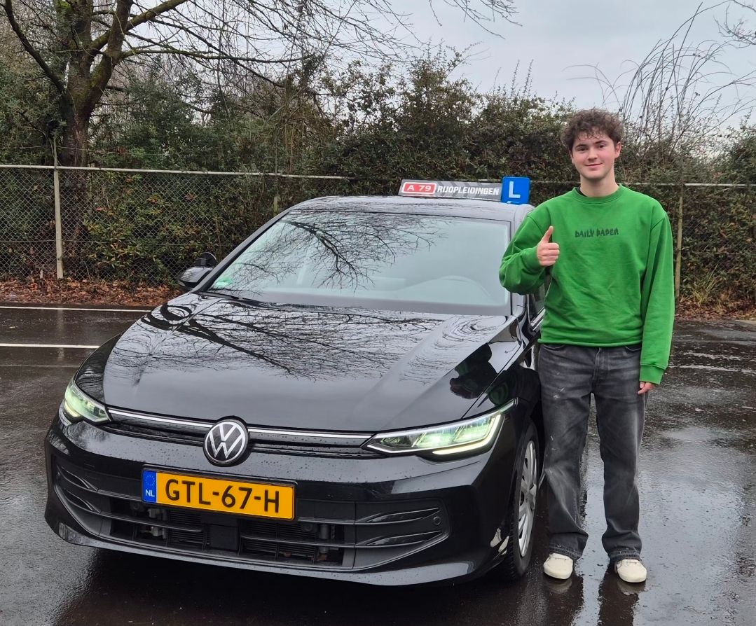Een man in een groene trui met zijn duim omhoog staat naast een zwarte auto met kenteken GTL-67-H en een 