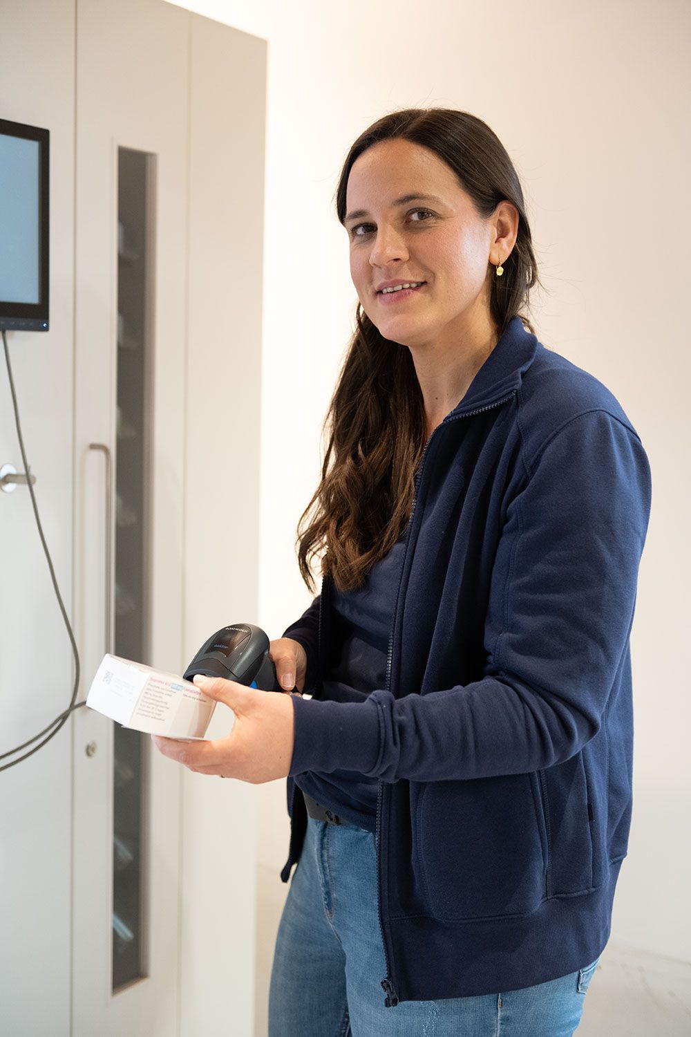Eine Frau in einer blauen Jacke hält ein Barcode-Lesegerät in der Hand.