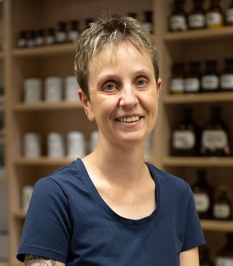 Eine Frau in einem blauen Hemd lächelt vor einem Regal voller Flaschen.