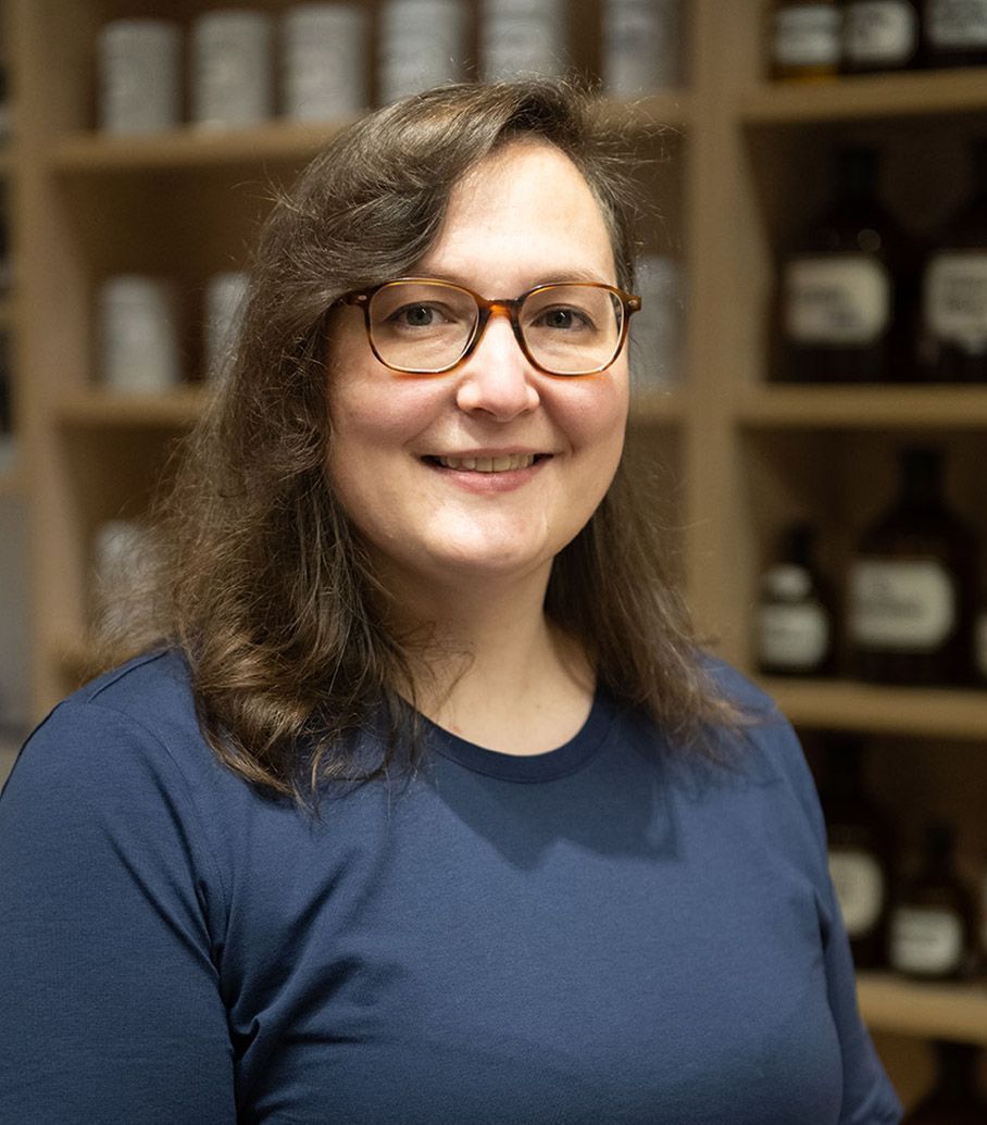 Eine Frau mit Brille und blauem Hemd lächelt in die Kamera.