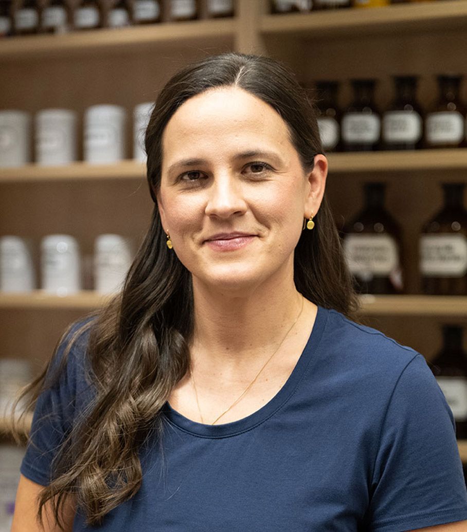 Eine Frau in einem blauen Hemd steht vor einem Regal mit Flaschen.