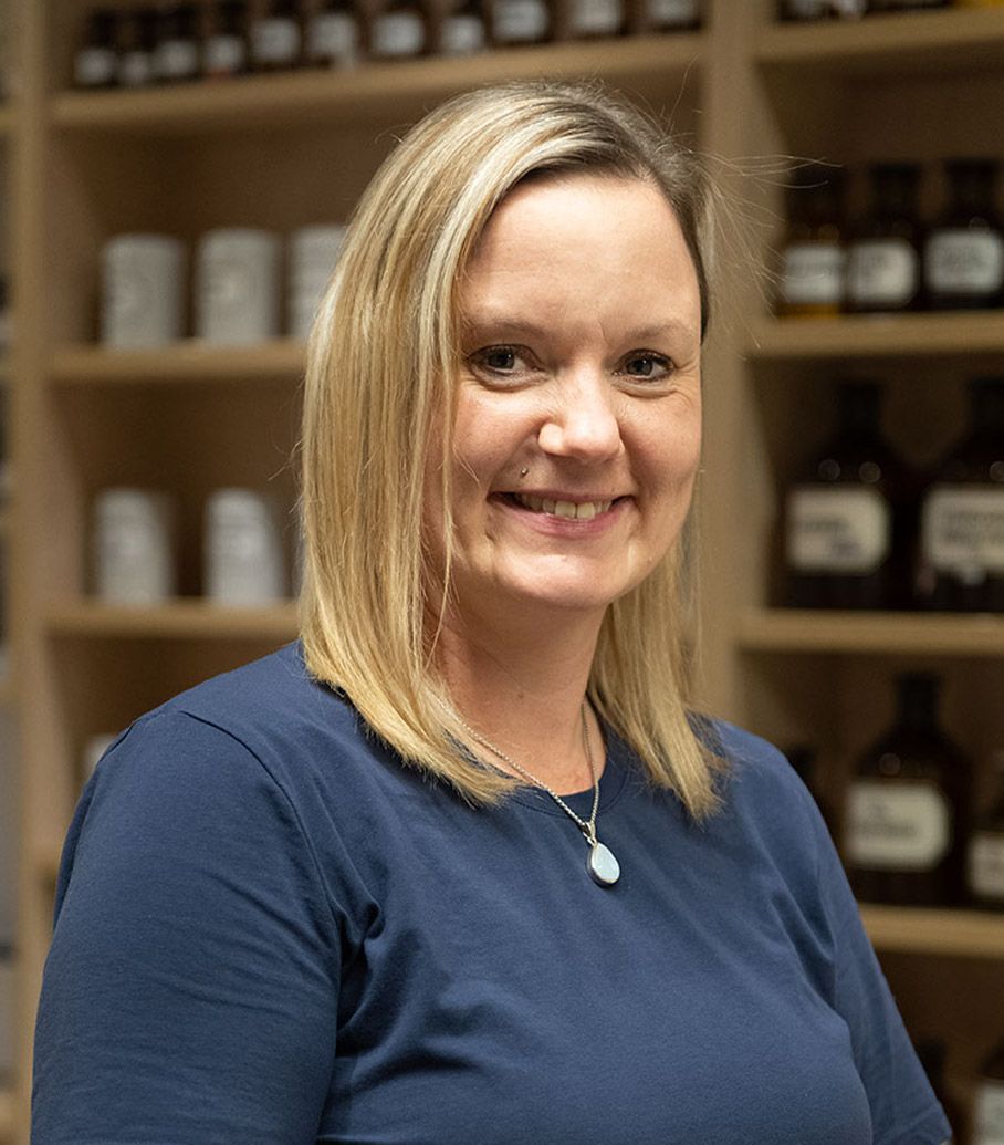 Eine Frau in einem blauen Hemd lächelt vor einem Regal voller Flaschen.