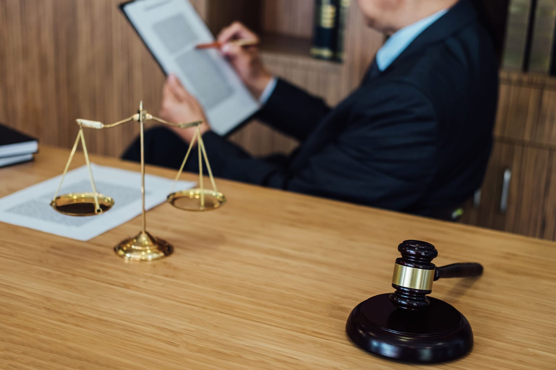 Lawyer in a suit reviewing documents with scales of justice and a gavel on a wooden desk