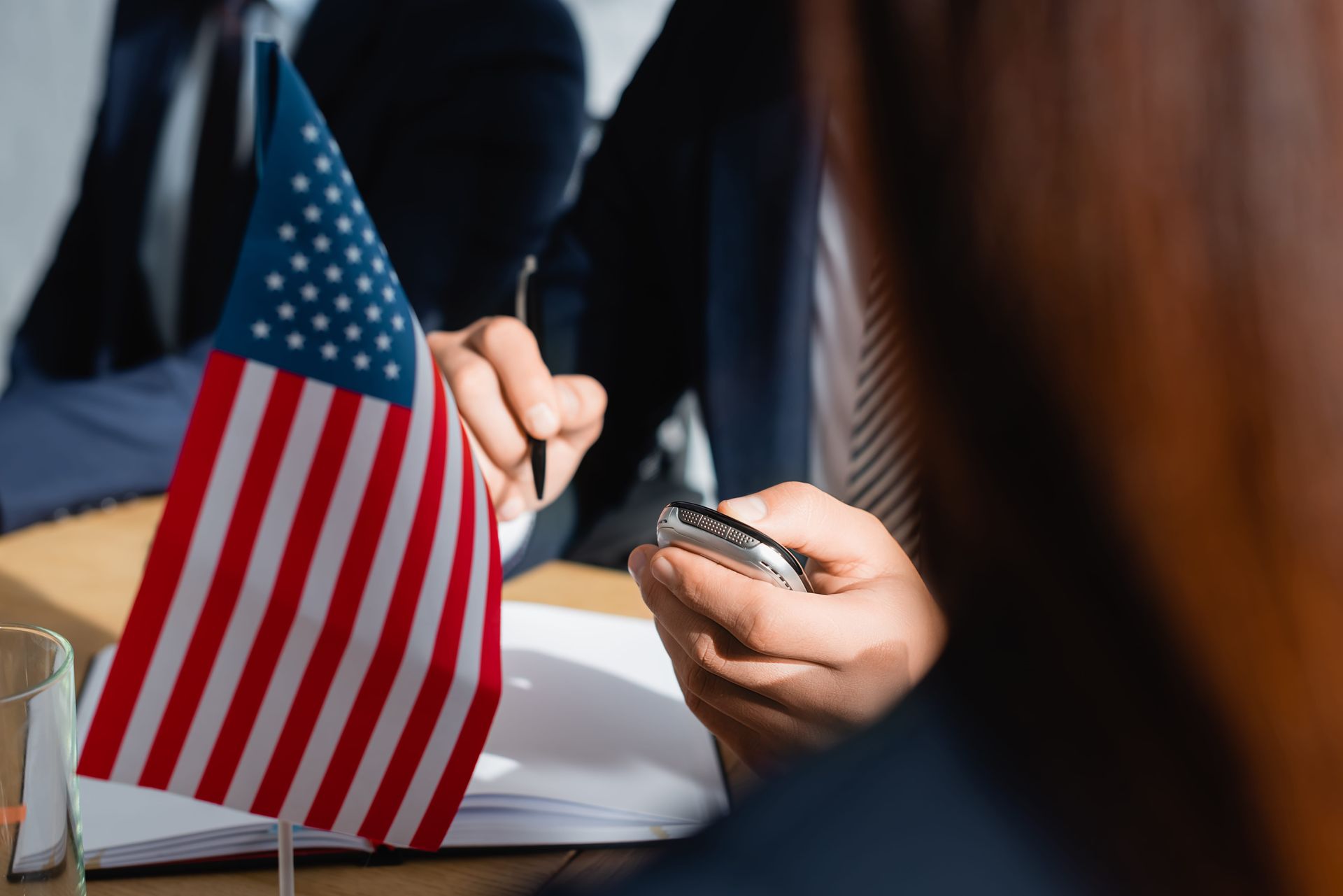 American flag on a table beside a person holding a smartphone during a meeting