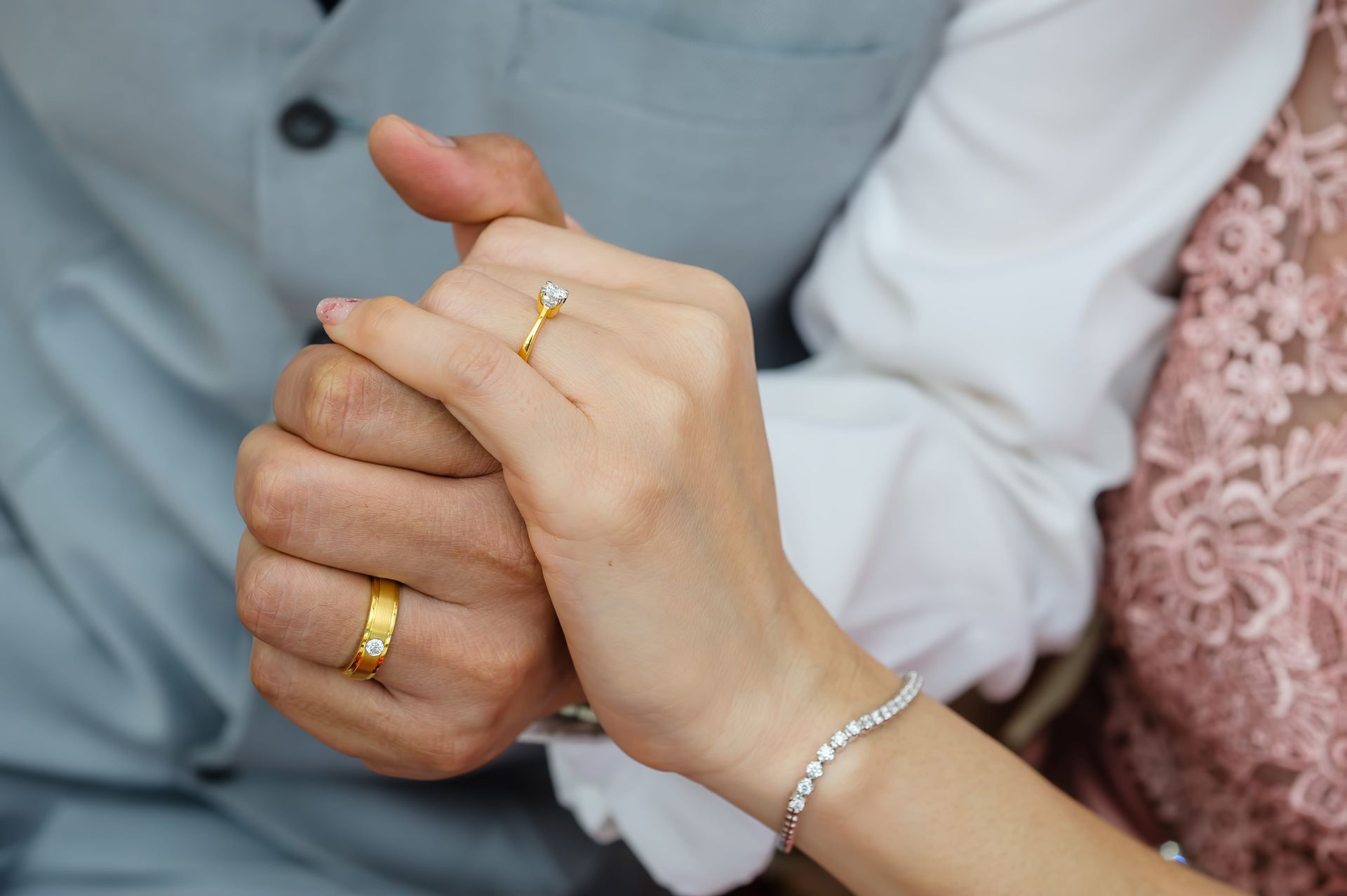 Hands with gold rings clasped together, resting on formal clothing