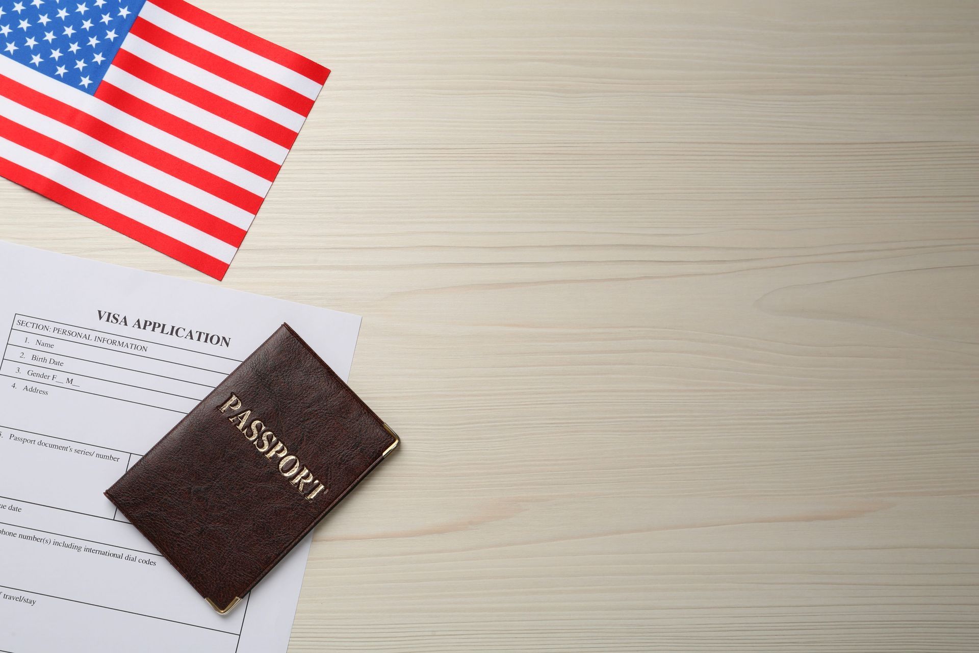 U.S. passport on a travel form beside a small American flag on a light wood desk