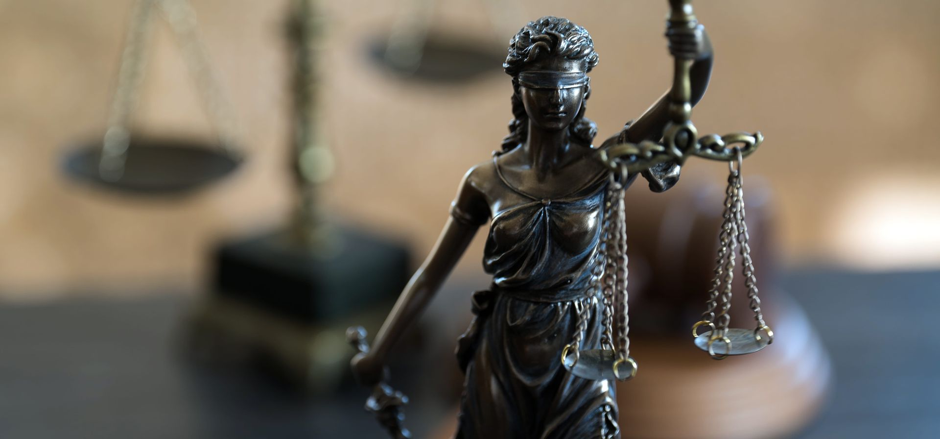 Bronze Lady Justice statue holding scales in a courtroom setting