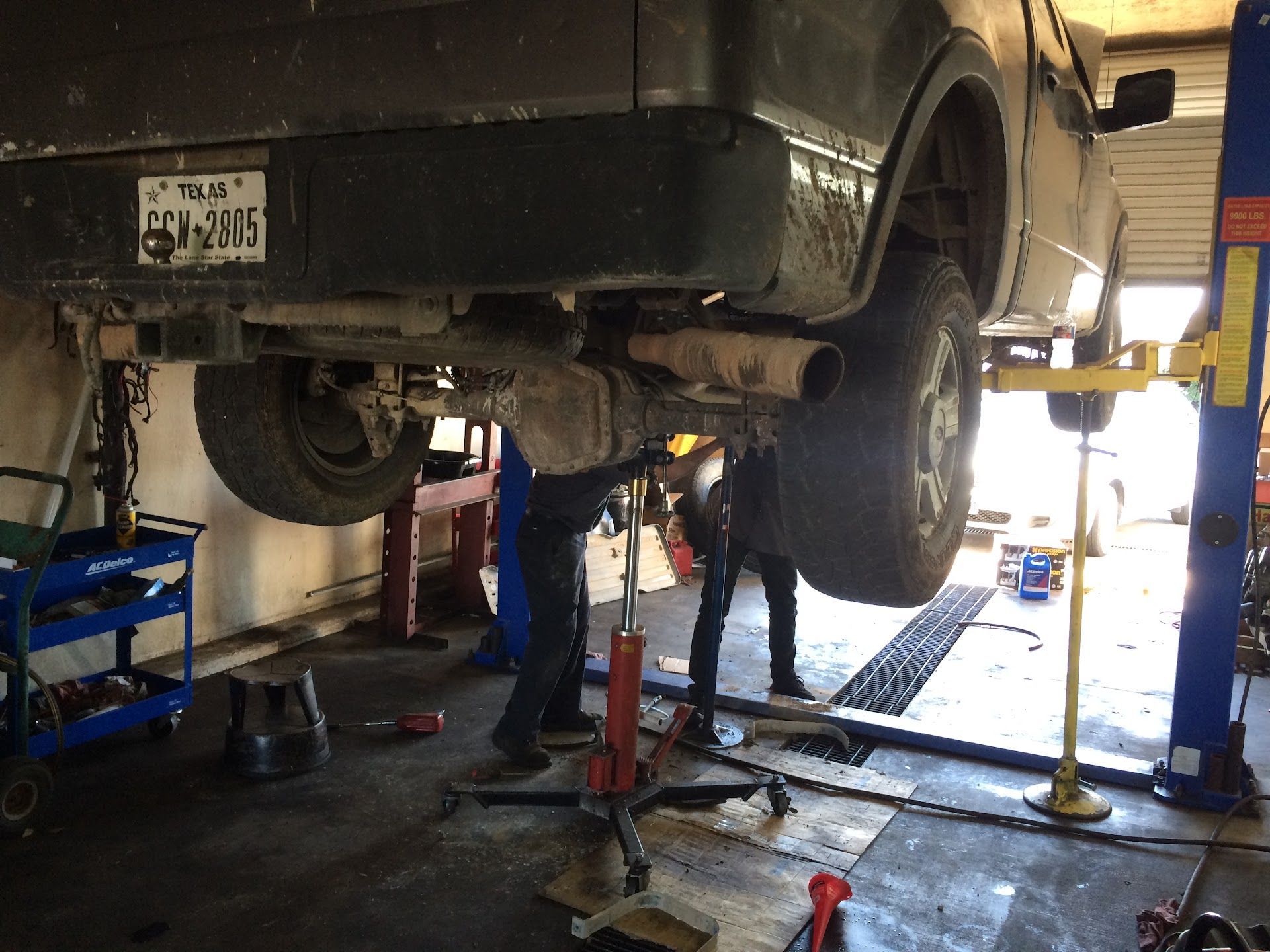 A truck raised on a lift in a repair shop; two people working underneath. | El Dorado Shell
