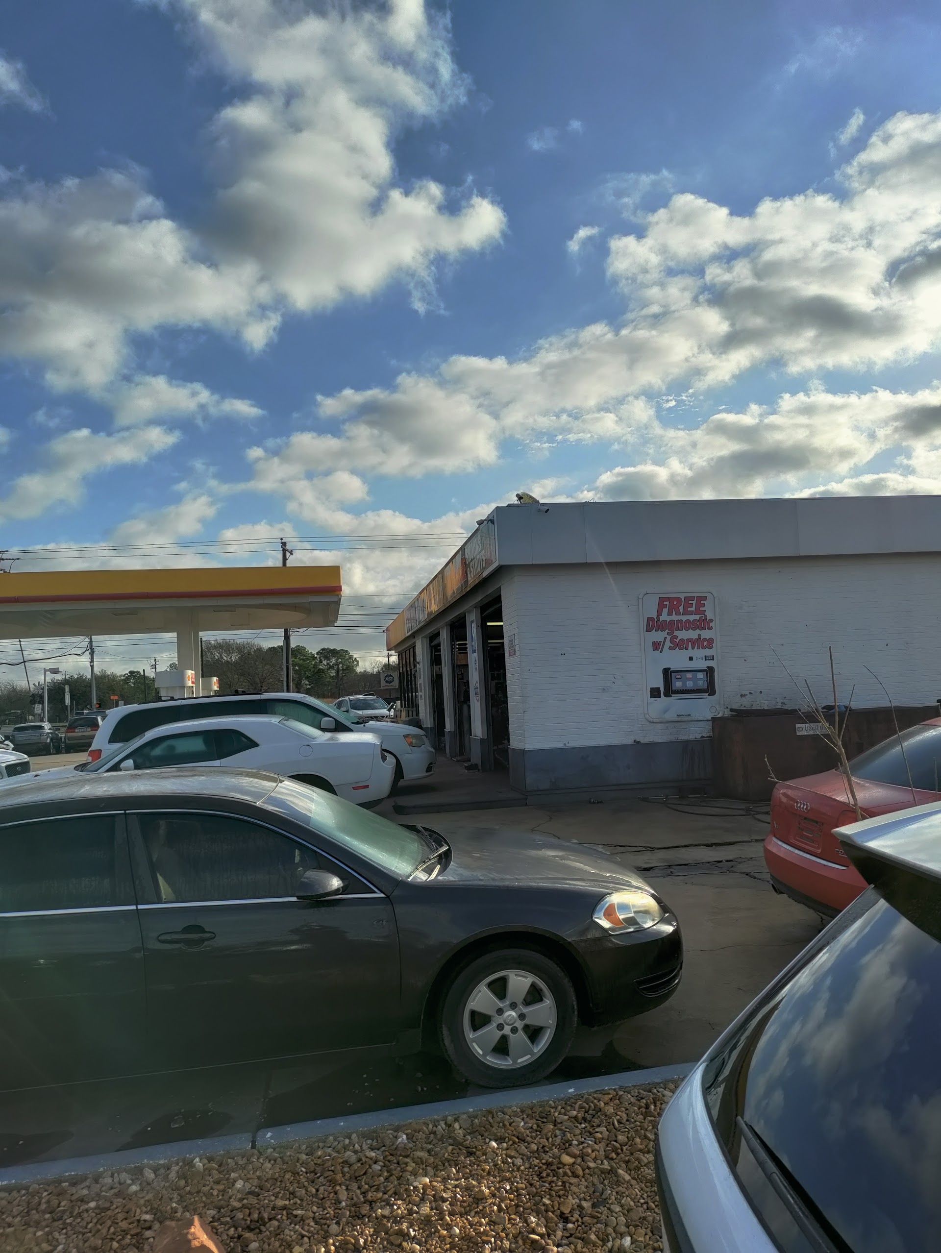 Shell gas station with cars parked in front. White building with black doors under a cloudy sky. | El Dorado Shell