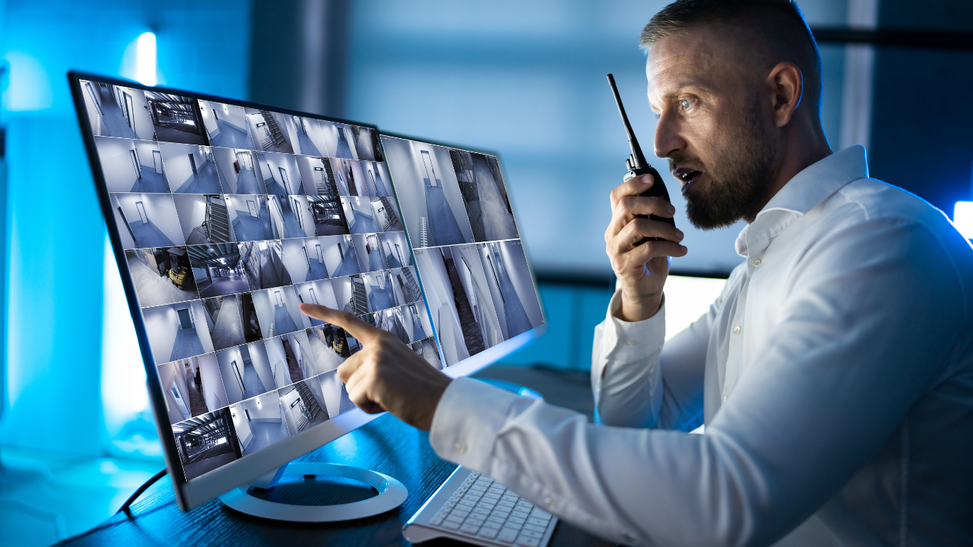 A man is talking on a walkie talkie while looking at a computer screen.