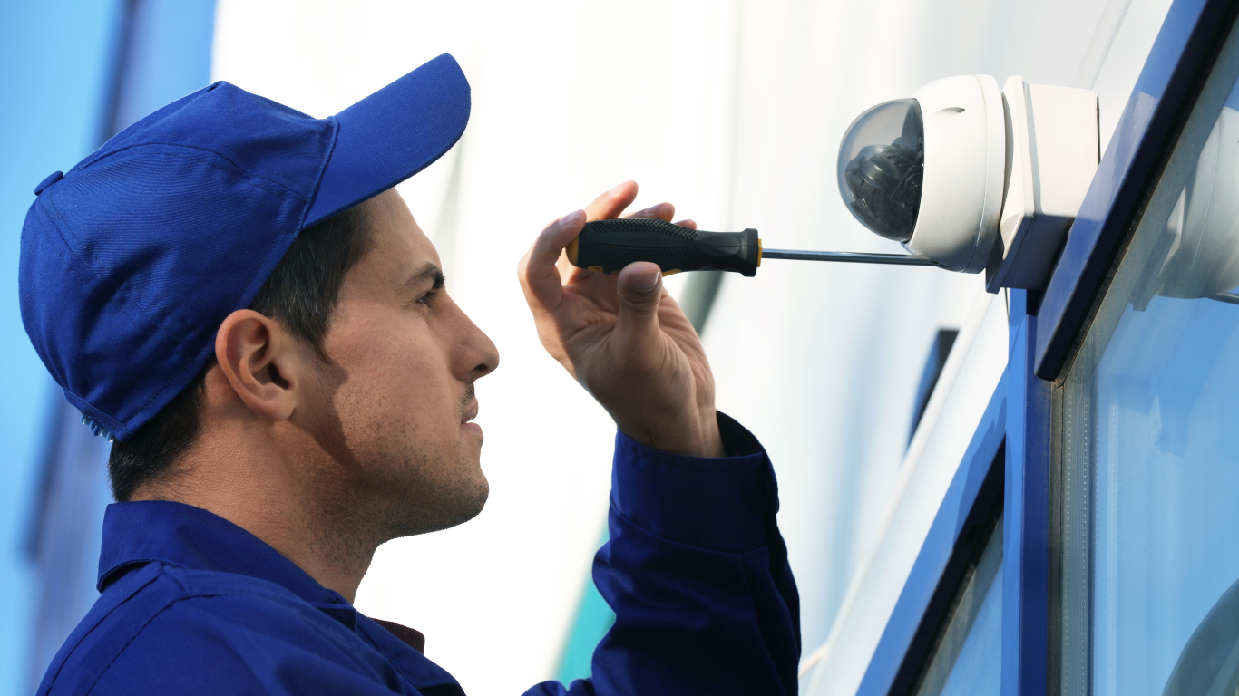 Security System Repair A man in a blue hat is fixing a security camera with a screwdriver.